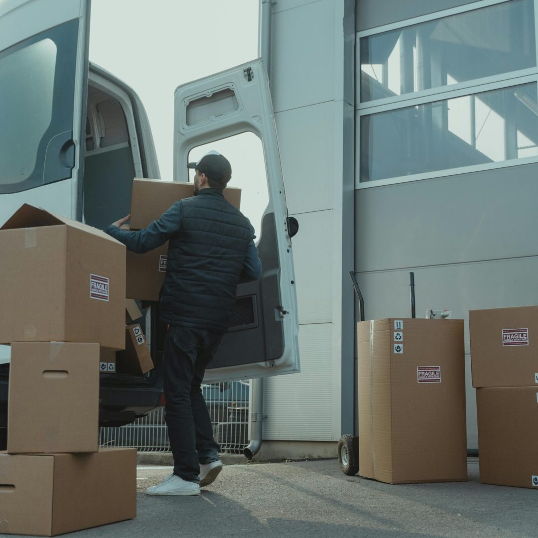pexels-photo-6169056-6169056 A delivery man unloading cardboard boxes from a van at a warehouse during the day.